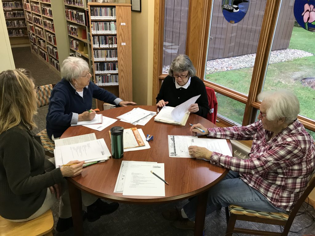 IMG_00991-1024x768 Four elderly individuals seated around a table in a library, engaged in discussion
