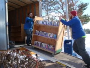 2 men pushing a cart of books onto a truck