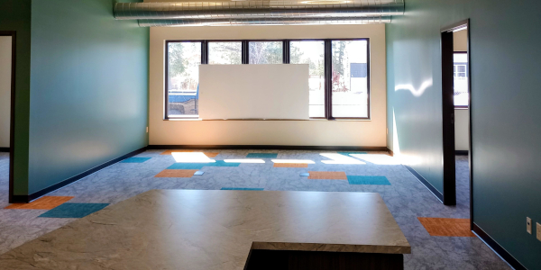 Empty room with green walls, windows, a white board, and patterned carpet.