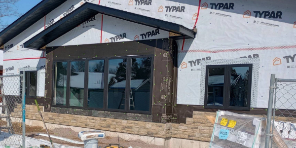 A building under construction with large windows and Typar wrap on the facade.